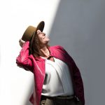 esempio di still life servizio fotografico negozio abbigliamento. Donna con cappello e giacca di pelle davanti ad un muro bianco in ombra